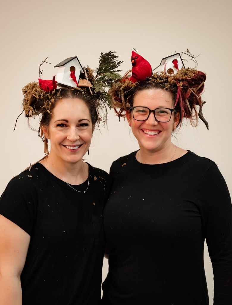 Two female staff wearing black shirts with birds nests and cardinals in their hair