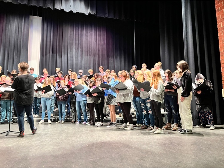 group image of many students standing on risers and looking at sheet music