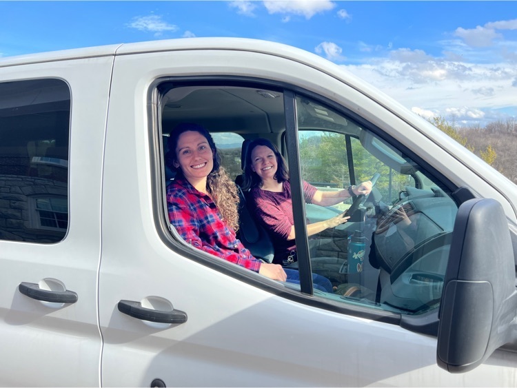 two women sit in the driver and passenger seats of a white van