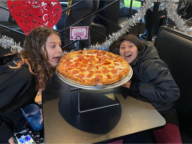 two girls pretend to take a bite out of a large pizza