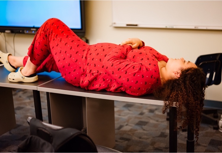 one student wearing pajamas pretends to sleep on a desk