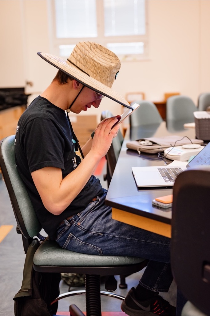 one male student wearing a safari hat and looking at his tablet