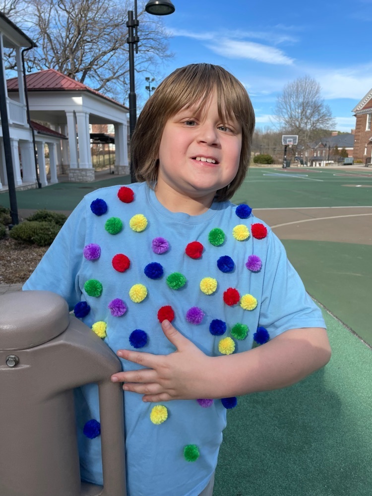 male student smiles while playing outside and showing his T-shirt adorned with fuzzy Pom Pom balls