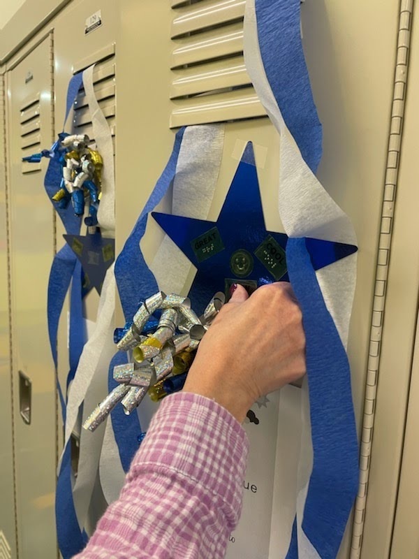staff places a large blue star on a student’s locker to add to the decorations. the star has braille stickers affixed 