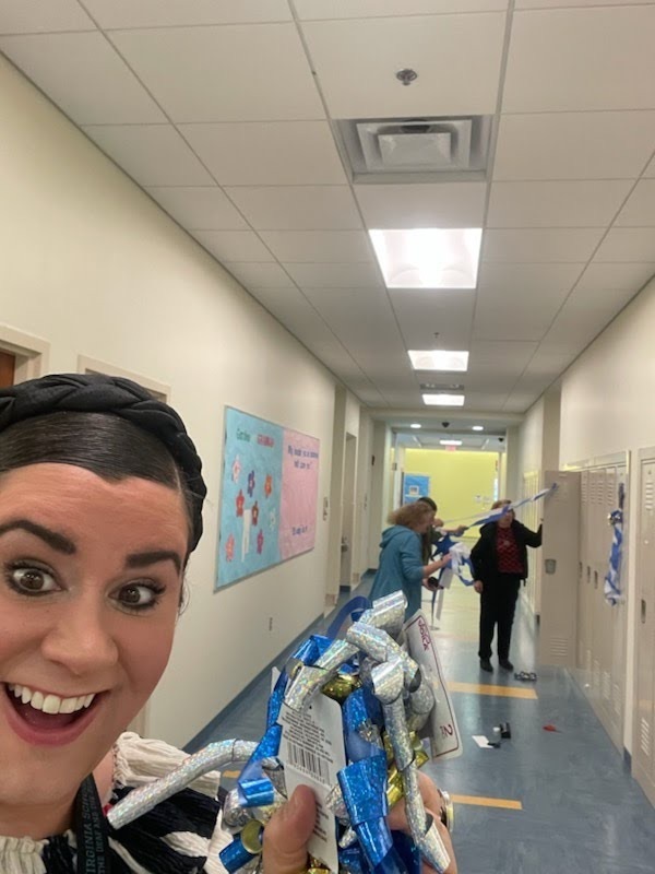 female staff holds decorations in a close up selfie while two other staff work on a locker further away from her