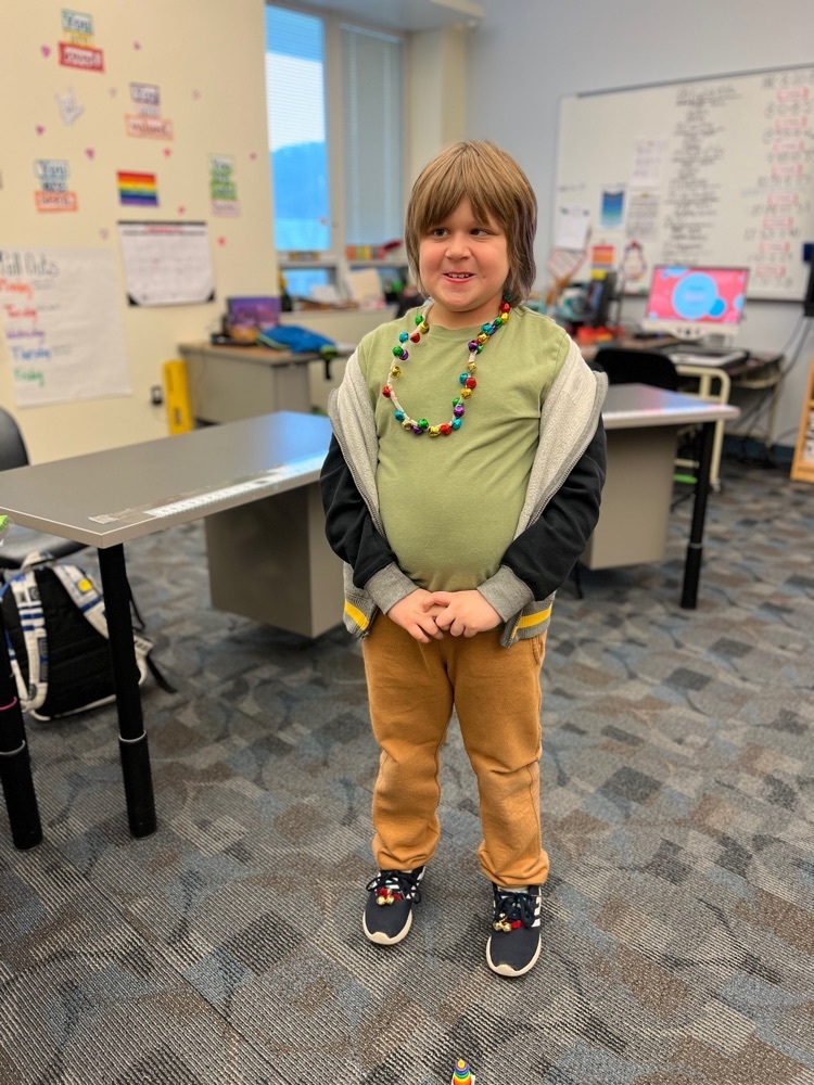 male elementary student wearing a necklace of bells and bells on his shoes standing in a classroom 