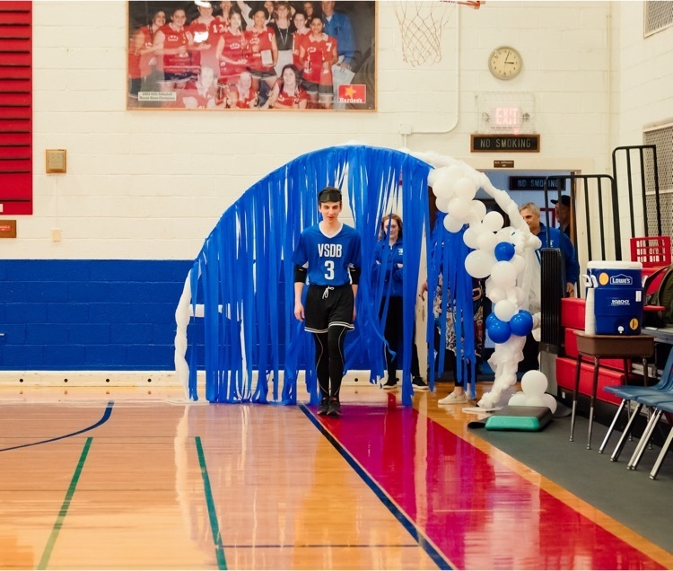 male student walking through a decorated arch with blue streamers across the front