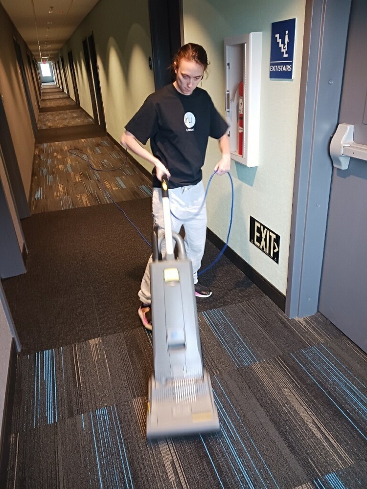 female student using a vacuum in a hallway