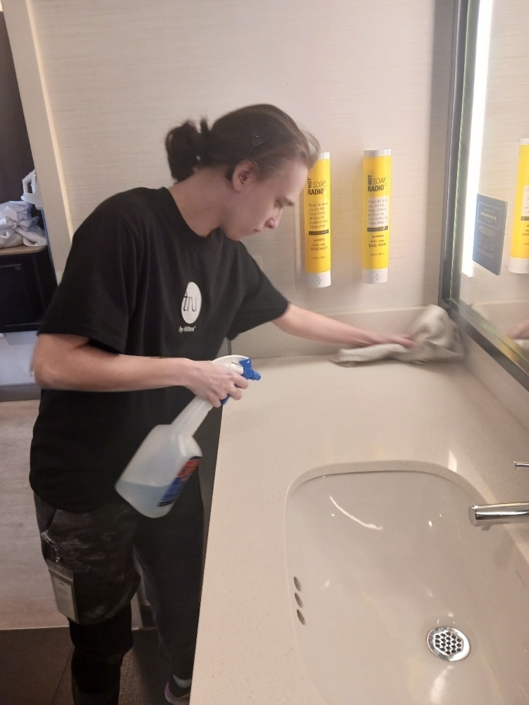 female student cleaning a bathroom sink and counter