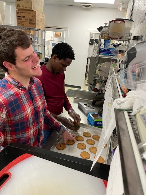 two students in a kitchen pulling cookies off a baking sheet