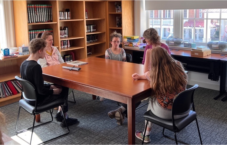 two staff sit at a table in the library with three students 