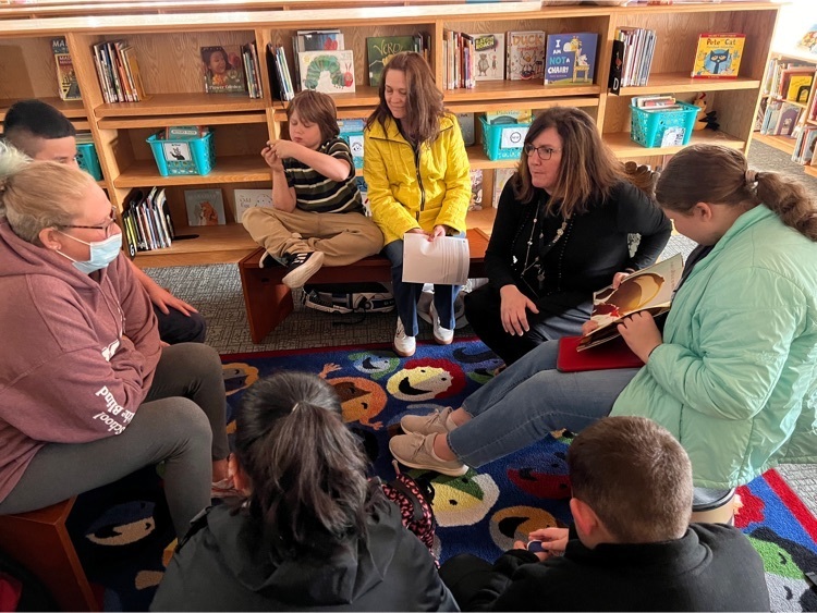 female staff reading a book to a group of elementary students 