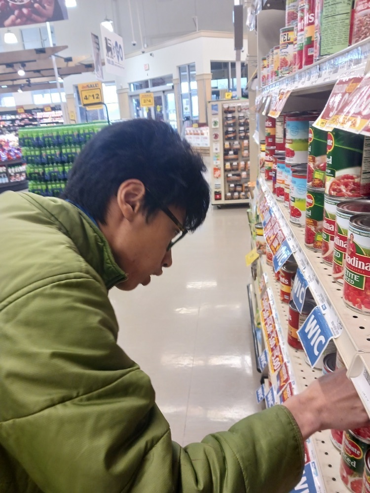 male student wearing a food lion uniform arranges a can on a shelf in the grocery store
