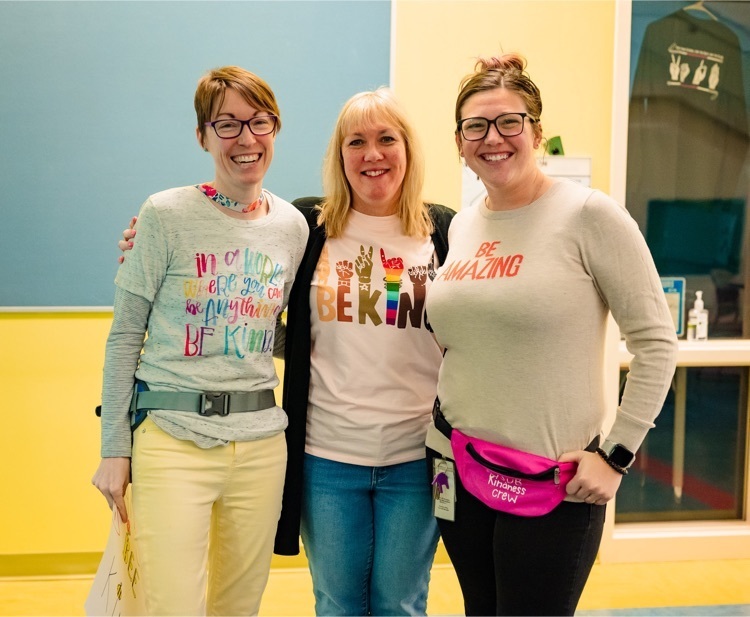 three female staff stand in the lobby showing off their kindness themed shirts 