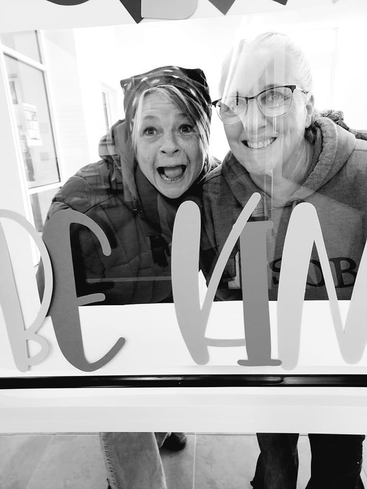 two female stand within a frame that says be kind. photo is in black and white