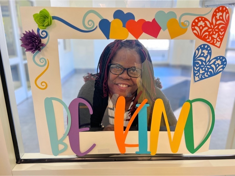 female staff smiles inside a frame that is decorated with many colors and has text saying “be kind” 