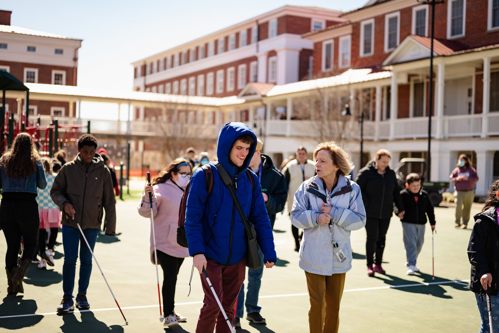 several students using white canes walking along the basketball court