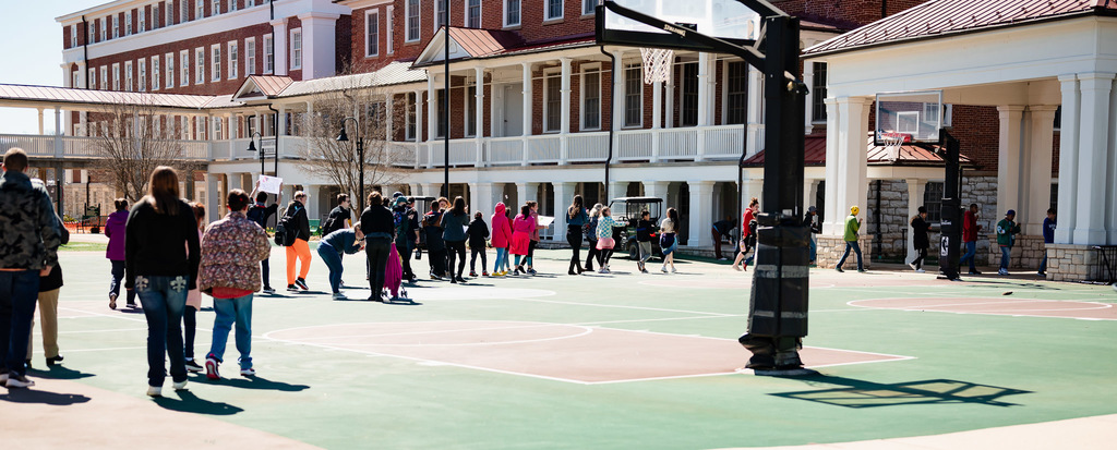 long line of students walk across the basketball court 