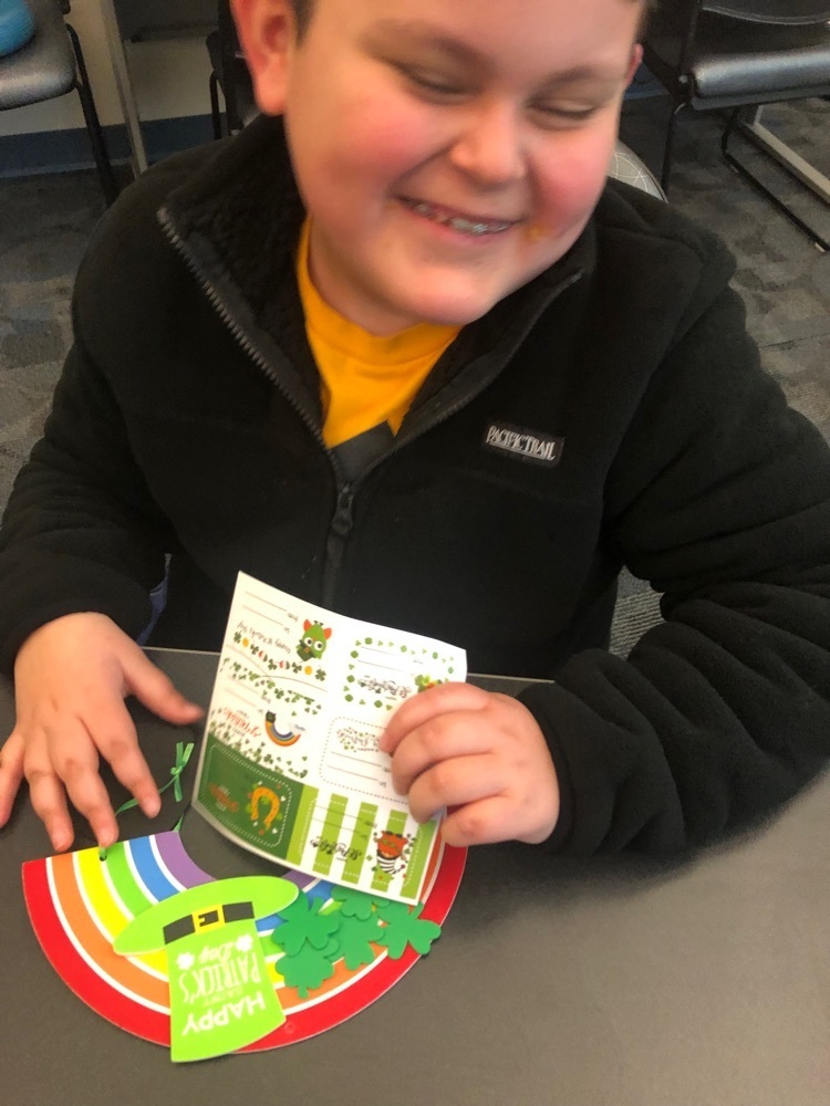 male student smiles with his rainbow craft on the desk in front of him