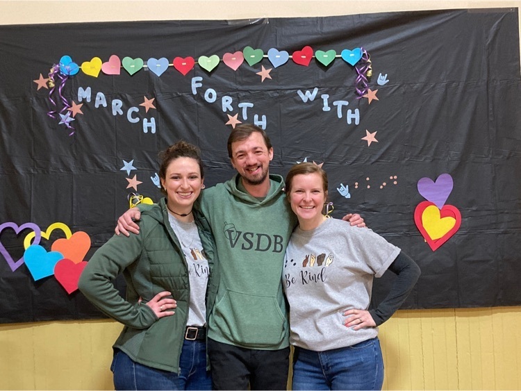 three staff stand in front of the kindness backdrop for a photo 