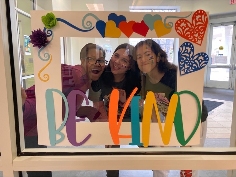 three students smile behind the be kind photo frame 