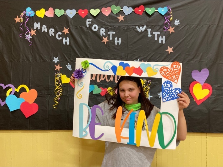 one student smiles behind the be kind photo frame