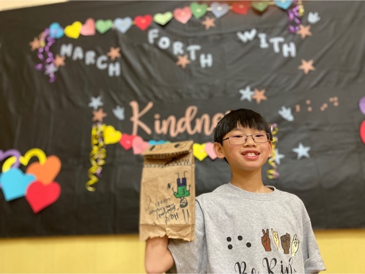 one student poses with his decorated bag in front of the kindness week backdrop 