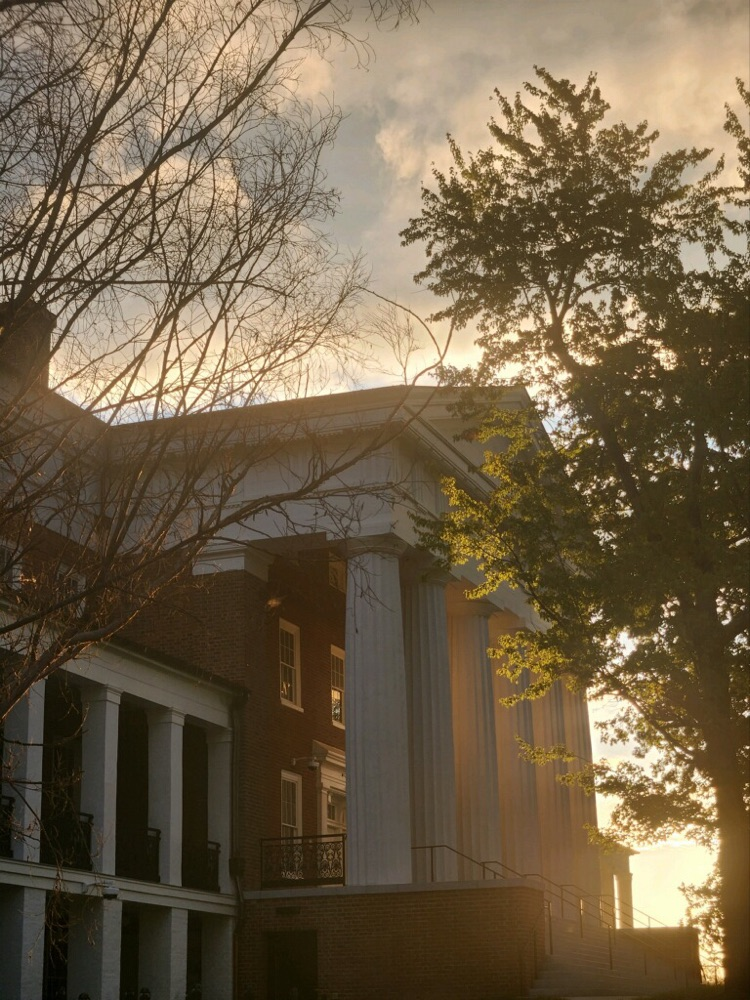 white columns of the main hall building with a sunrise creeping up from behind the building and surrounding trees