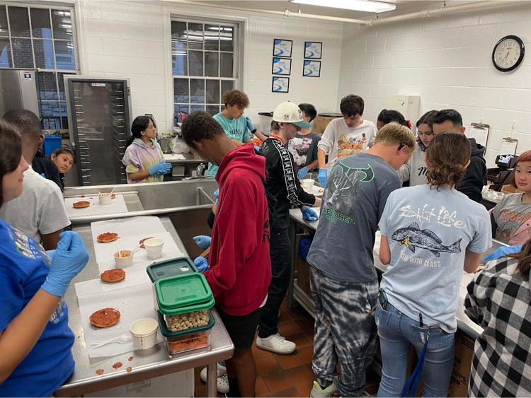 students and staff in the kitchen bent over their pizza bagels in progress 