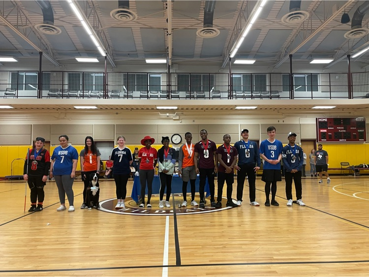 many goalball players lined up in the gym, wearing their school jerseys, some with a medal around their neck 
