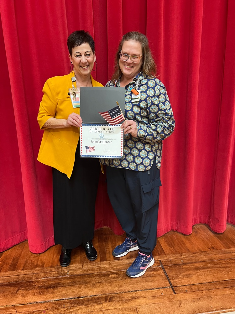 Jennifer and Pat together with Jennifer’s certificate, ribbon, and American flag